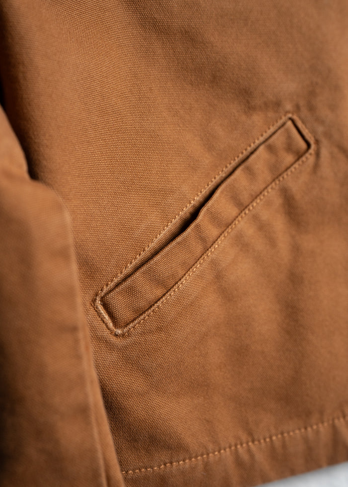 Close-up of a brown fabric jacket pocket with detailed stitching, showcasing texture and craftsmanship in natural light.