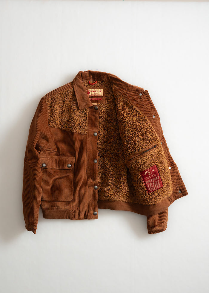 Brown corduroy jacket with a soft fleece lining, open to reveal a red label. The jacket features buttoned pockets and cuffs.