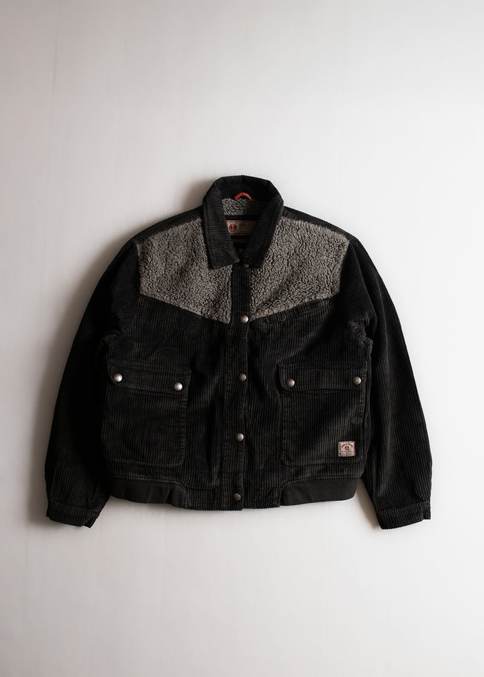 Black corduroy jacket with gray fleece yoke, buttoned pockets, and collar, displayed on a white background.