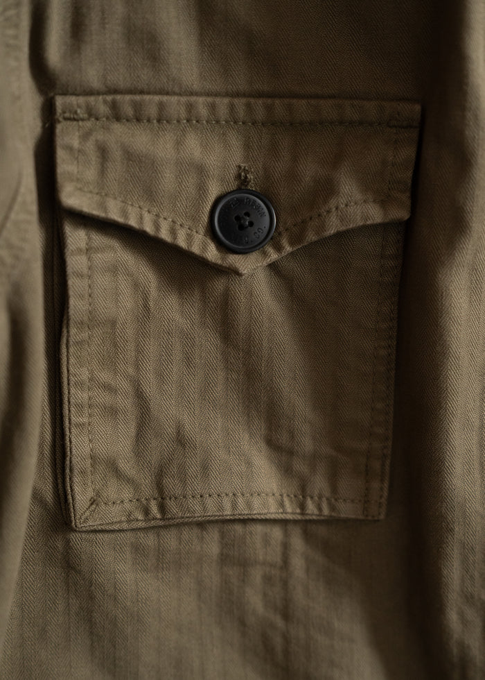 Close-up of a khaki shirt pocket with a black button, highlighting the fabric texture and stitching details.