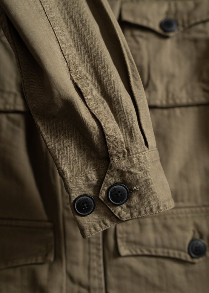 Close-up of a khaki jacket sleeve with black buttons, highlighting its detailed stitching and textured fabric.