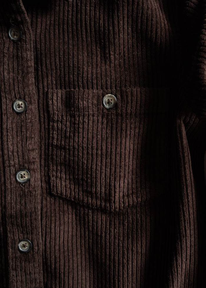 Close-up of a brown corduroy shirt with vertical ridges, featuring a front pocket and four buttons, highlighting its texture.