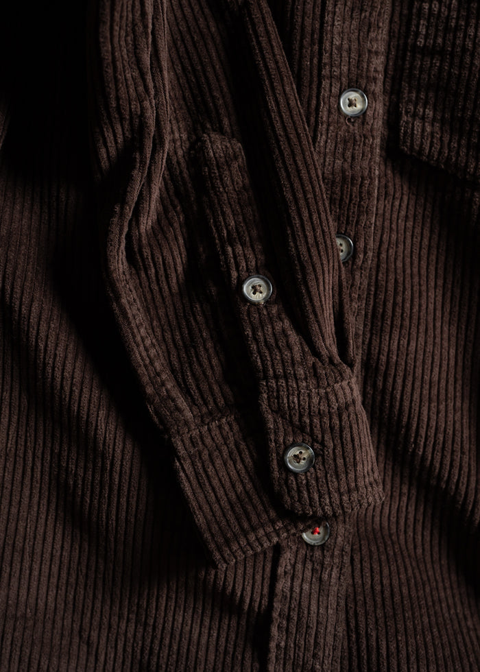 Close-up of a brown corduroy shirt with visible buttons, showcasing the textured fabric and rich color in detail.