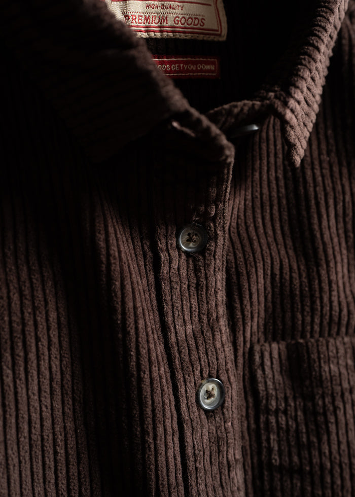 Close-up of a brown corduroy shirt with buttons and a visible label reading "Premium Goods." The texture is prominently featured.