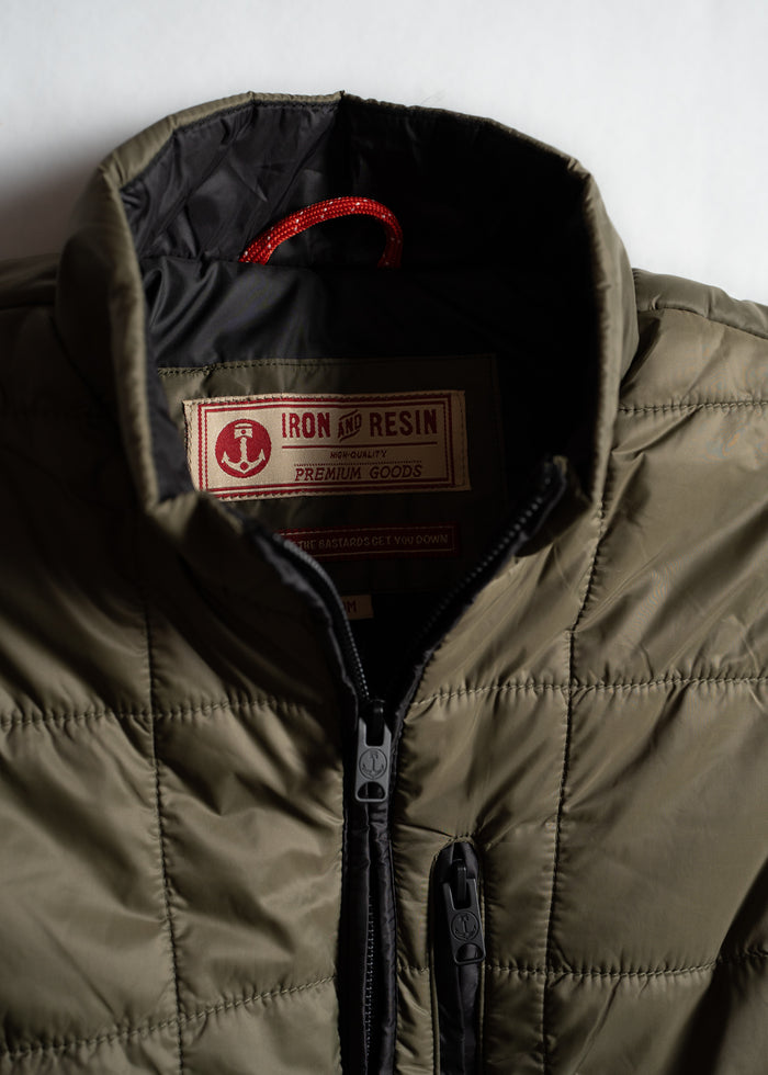 Close-up of an olive quilted jacket with a visible "Iron and Resin" label inside, highlighting premium quality and design.