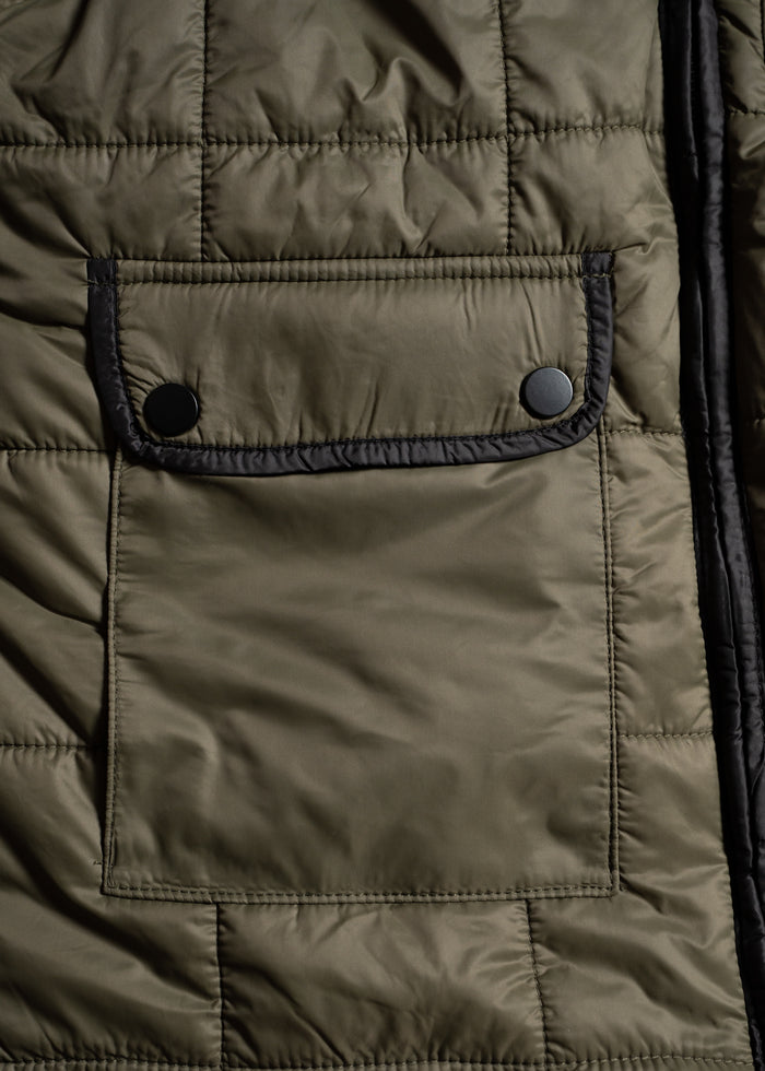 Close-up of a quilted jacket's olive green pocket with black trim and two black buttons, emphasizing texture and design.