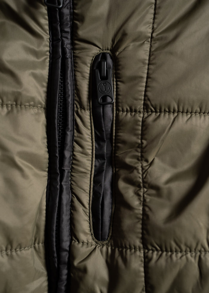 Close-up of a green quilted jacket with a black zipper and pocket, highlighting the texture and stitching details.