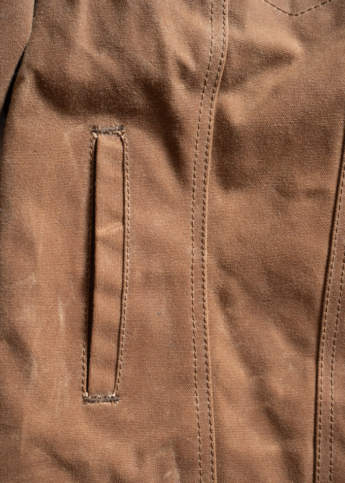 Close-up of a brown fabric jacket with visible stitching and a vertical pocket on the left side.