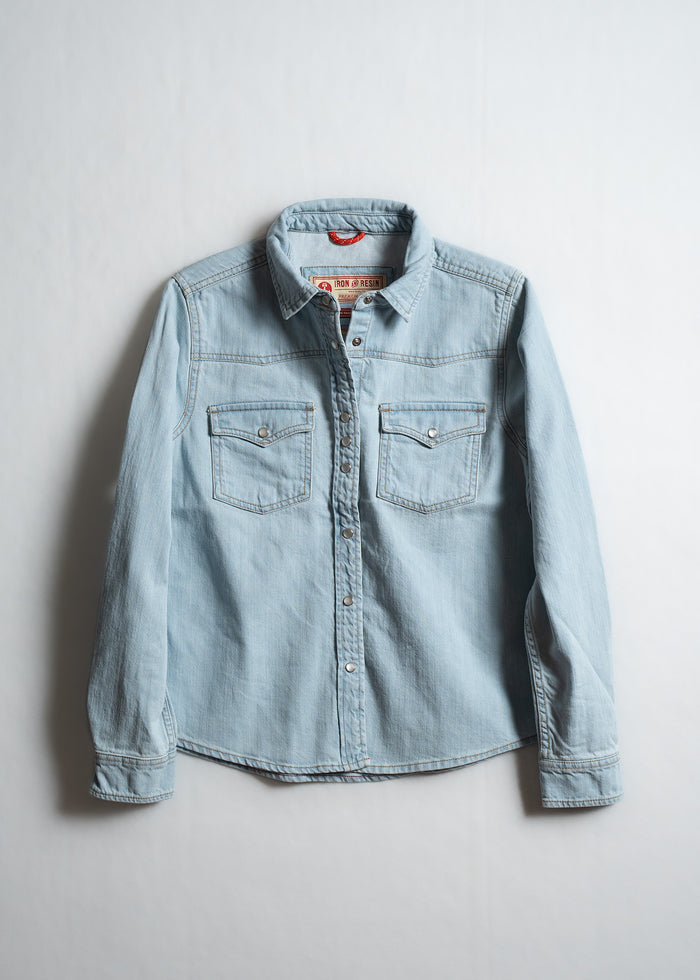Light blue denim shirt with button-up front and two chest pockets, displayed against a plain white background.