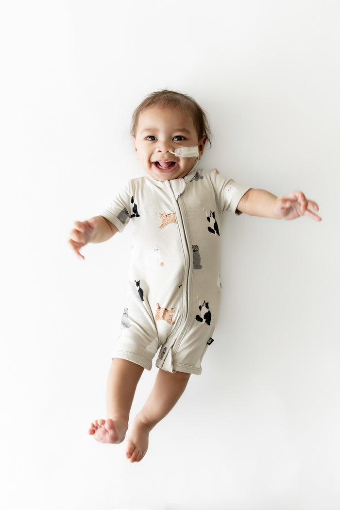 Smiling infant wearing the Zipper Shortall Romper in Fluffy Cat