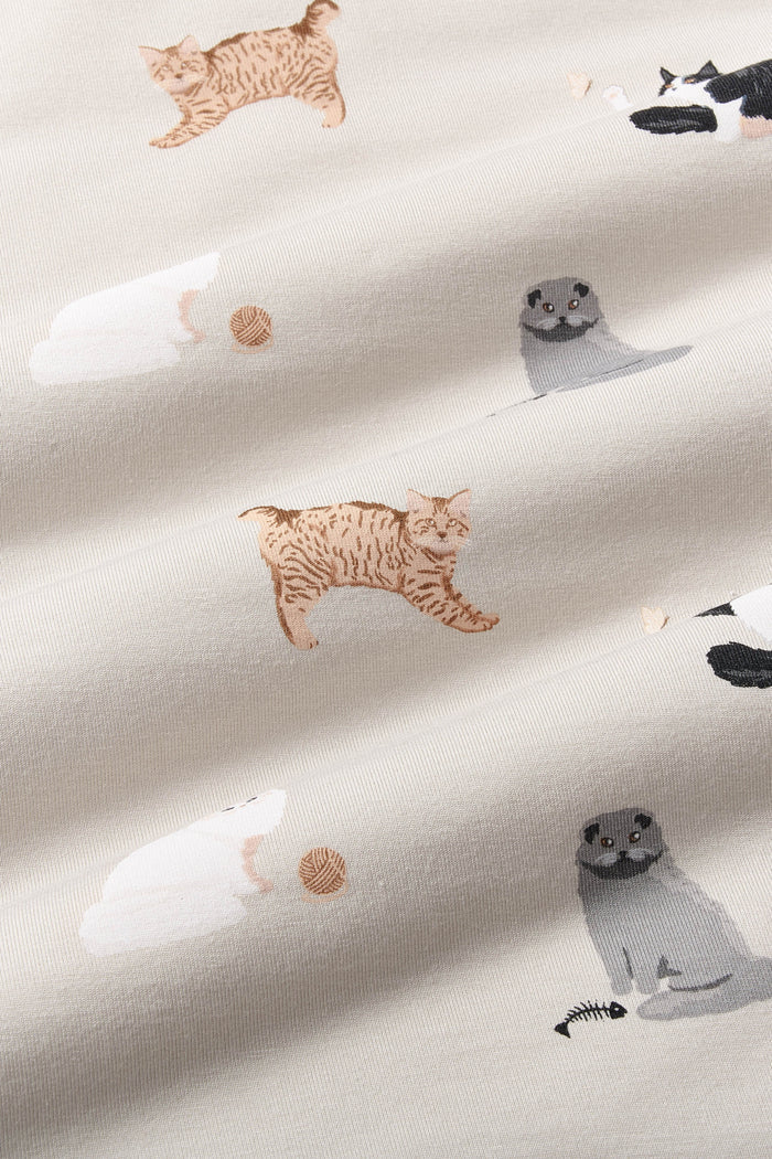 Close up of bamboo fabric: A repeating, all-over print featuring: a fluffy white cat next to a light brown ball of yarn; a fluffy grey cat with folded ears next to a black fishbone; a fluffy brown tabby cat stretching its front legs; a fluffy black-and-white cat batting at a white butterfly, over a warm grey background color called Oat.