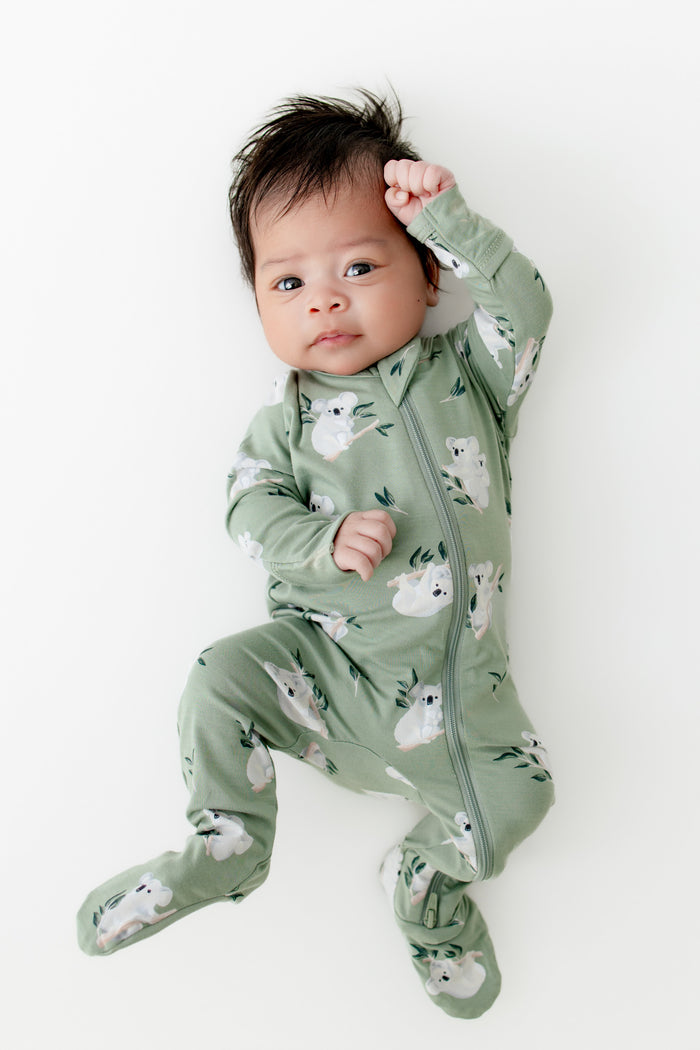 Newborn laying on a white surface wearing the Zippered Footie in Koala
