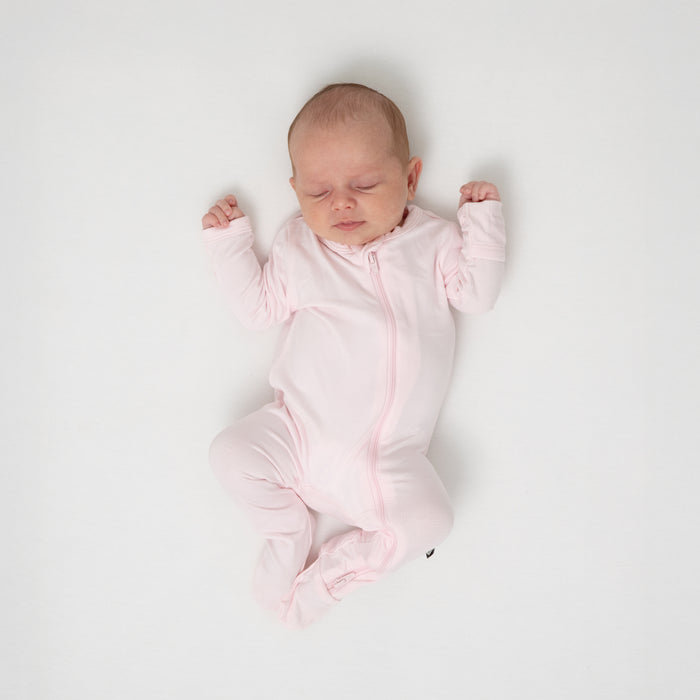 Sleeping infant wearing the Zippered Footie in Sakura with her arms up b her shoulders