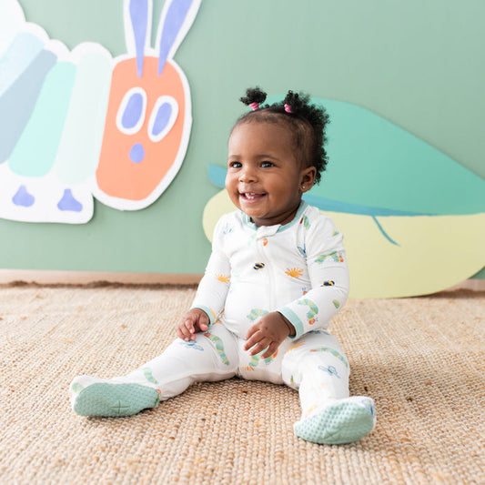 Toddler sitting on the floor wearing the Zippered Footie in The Very Hungry Caterpillar™ and Friends