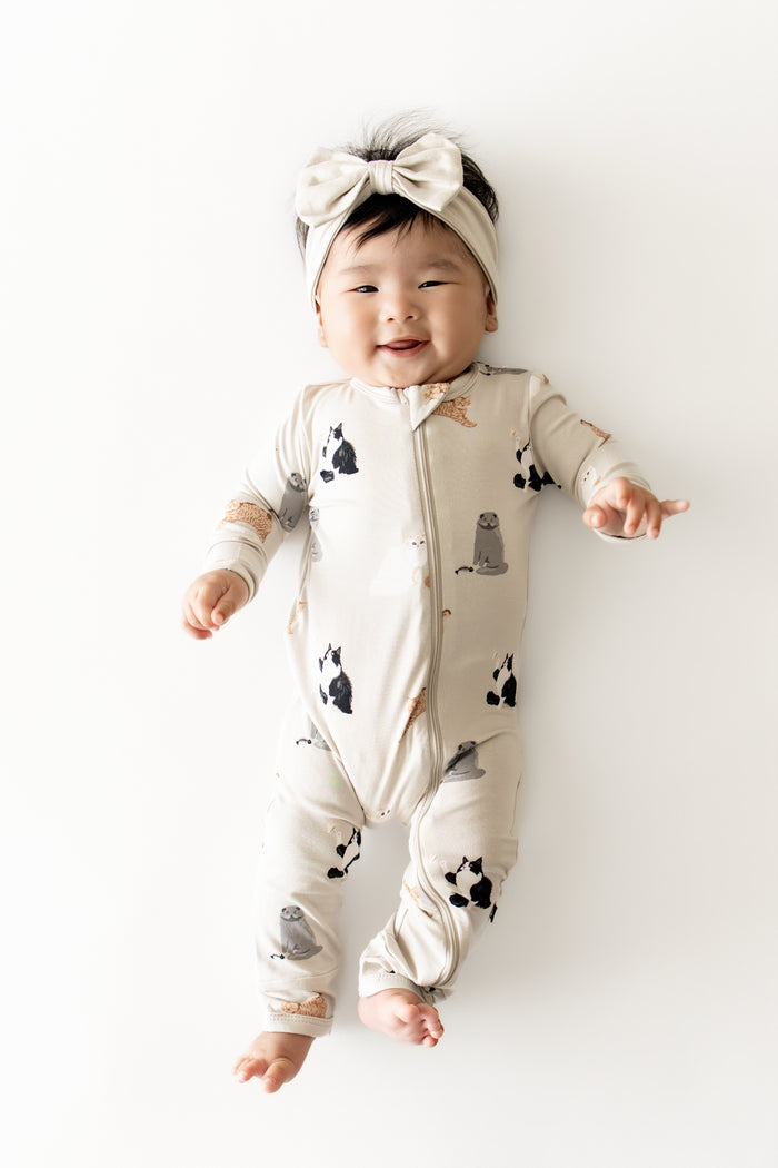 Infant girl wearing the Zippered Romper in Fluffy Cat with light beige bow